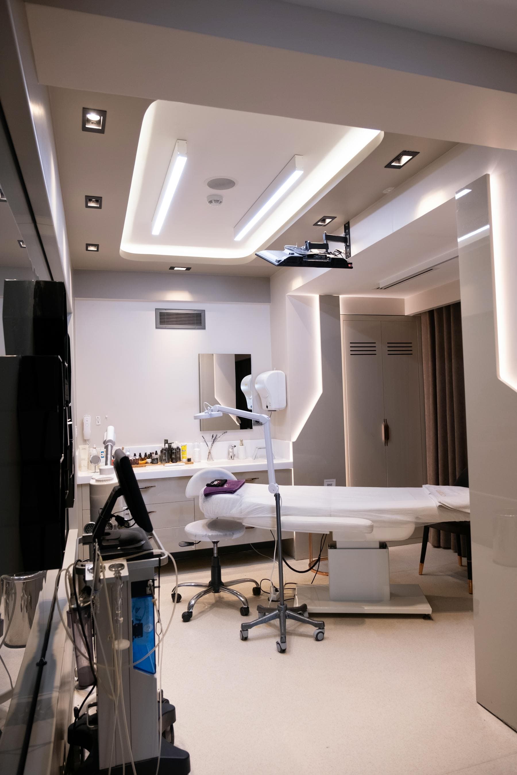Modernes, hell ausgeleuchtetes Behandlungszimmer mit Behandlungsliege und Gerätewagen — beispielhaft für ein professionell eingerichtetes Laserstudio.